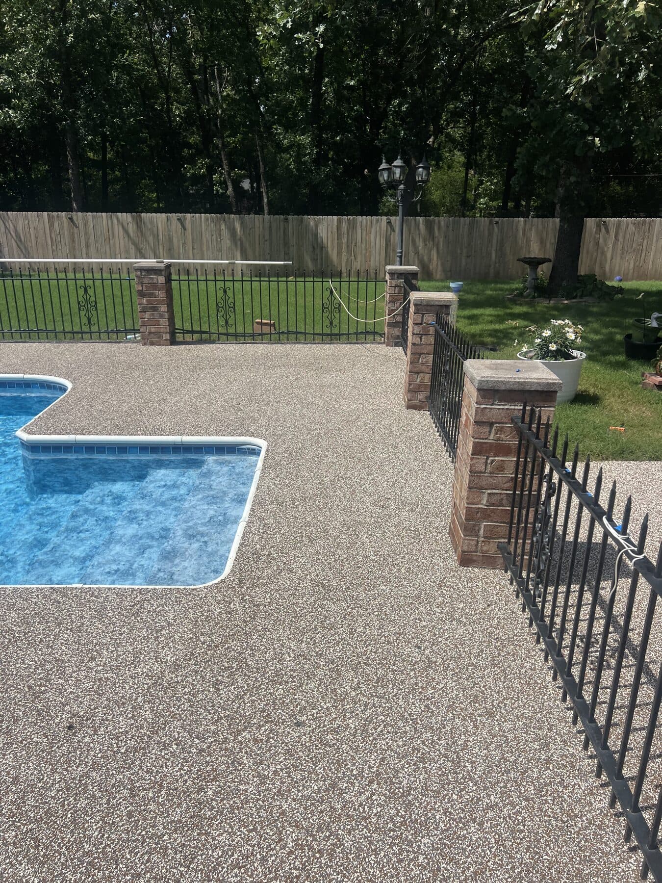 Finished Brownstone pool deck bordered by brick columns in Cabot