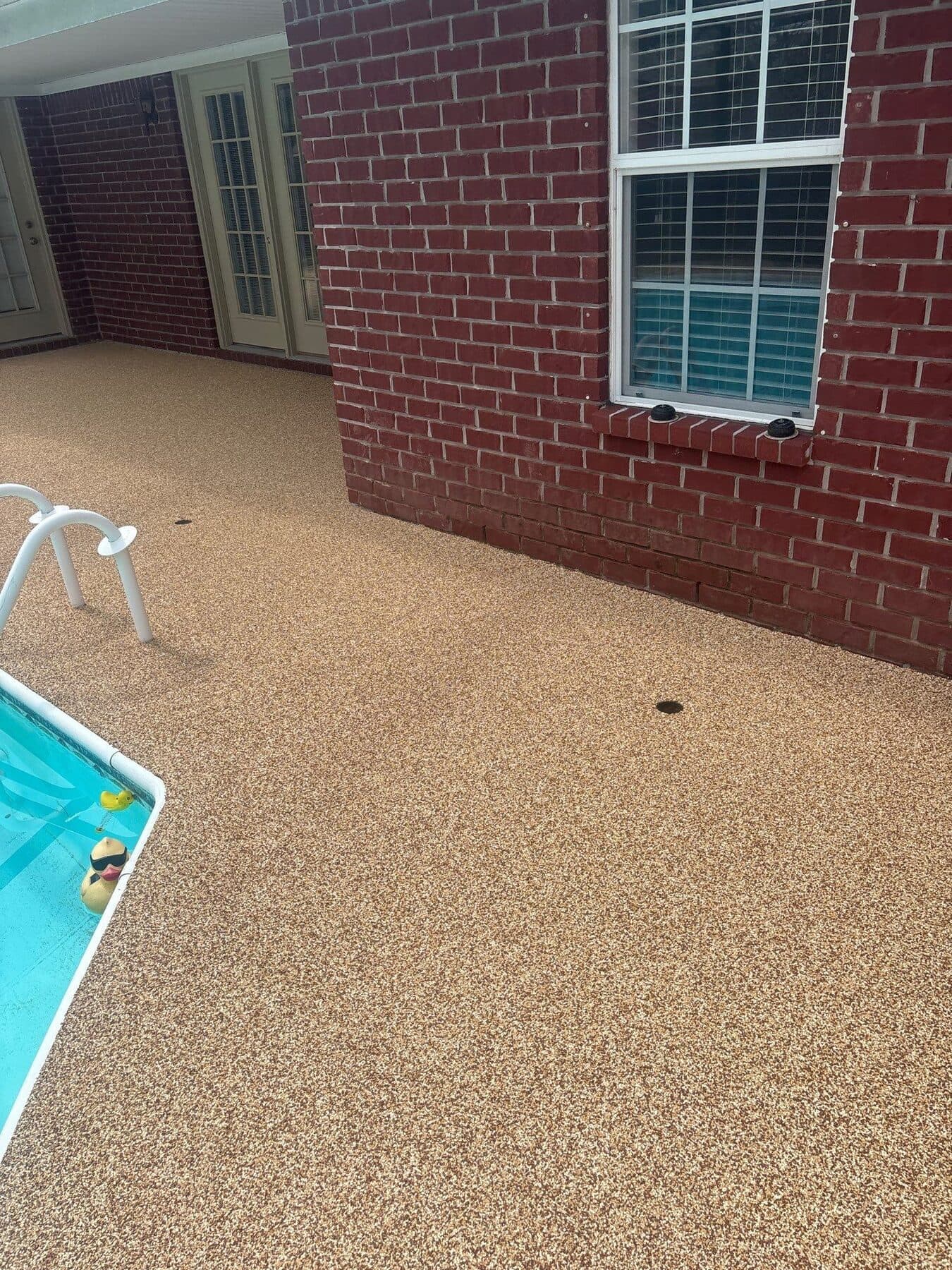 Finished warm neutral pool deck beside a covered patio