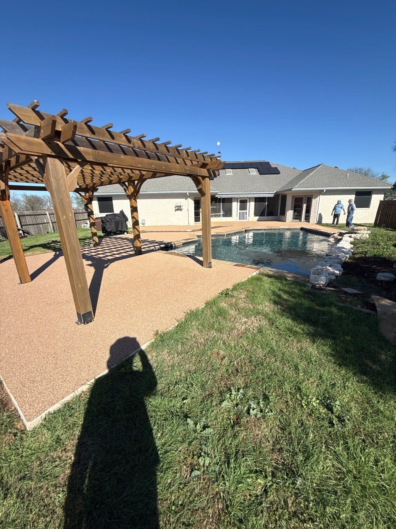Finished warm pool deck beneath a backyard pergola