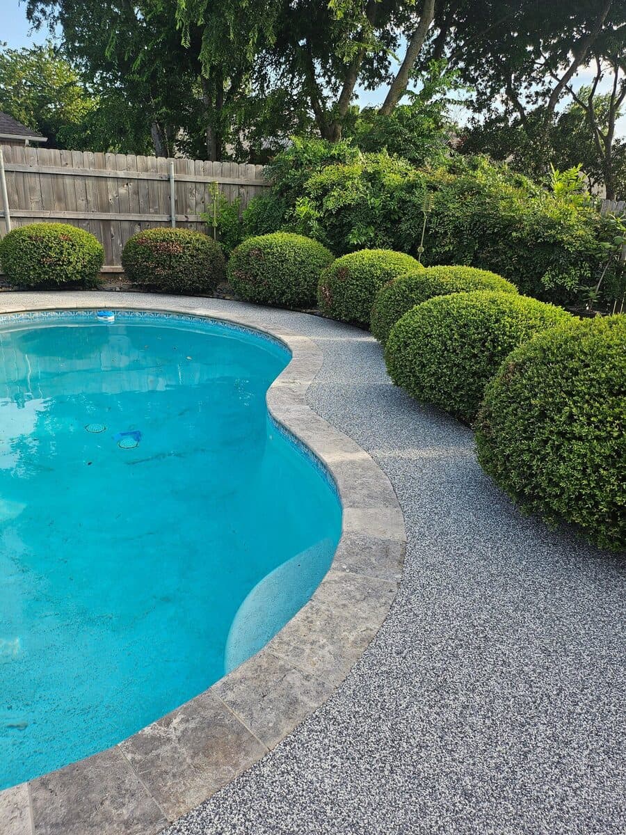 Finished Nickel pool deck bordered by sculpted green hedges